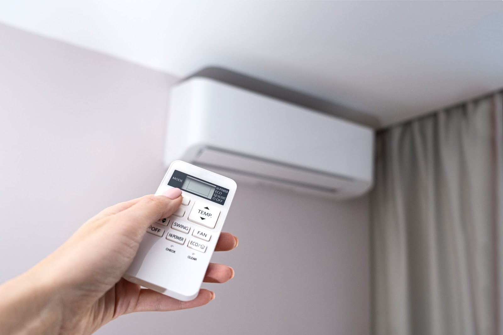 A hand is shown using a remote control to adjust the temperature settings of a ductless AC unit.
