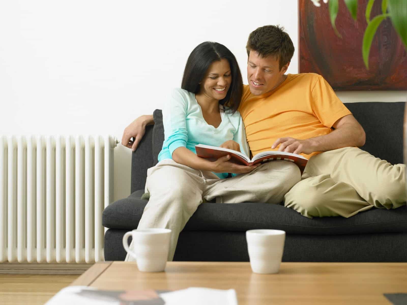 Couple sitting on a couch next to a heater. 