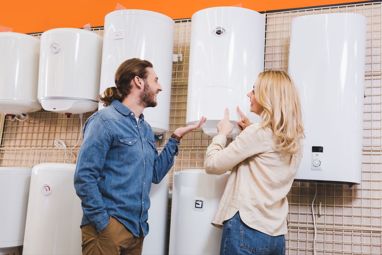 A couple in a store smiling at each other while gesturing towards tankless water heaters on display.