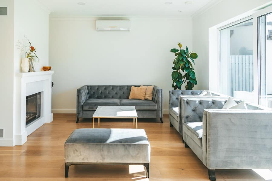 View of a living room with couches, hardwood floors, and a fireplace with an air conditioning unit on the wall near the ceiling.