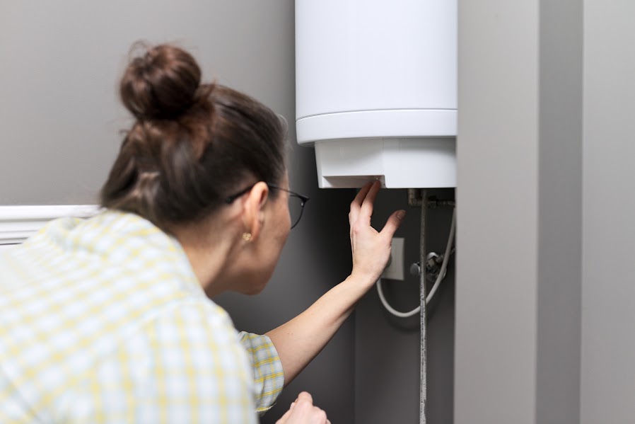 A woman with glasses bending over to check the temperature on a tankless water heater. 